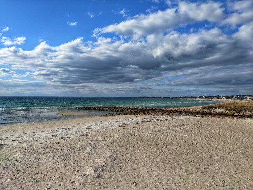 A serene beach scene with soft sand, gentle waves, and a cloudy sky over the calm ocean.