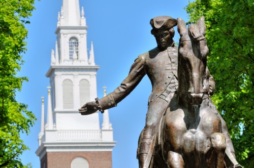 A bronze statue of a man on horseback with a church steeple in the background, surrounded by green trees.