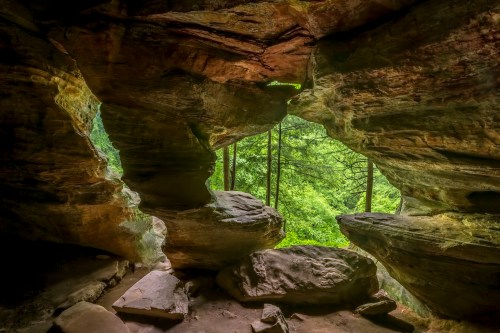 A view from inside a cave, showcasing rocky formations and lush green trees outside.