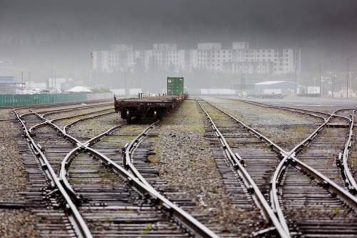 A foggy railway yard with multiple tracks diverging, leading to distant buildings and containers.