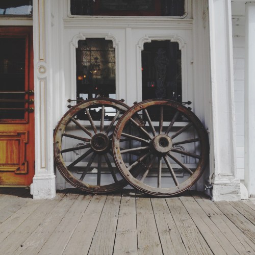 Two vintage wooden wheels leaning against a building, with a wooden door visible in the background.
