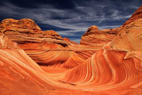 Vibrant, swirling sandstone formations in a desert landscape under a blue sky with wispy clouds.