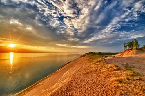 A serene landscape at sunset, featuring a sandy shore, calm water, and dramatic clouds reflecting the golden light.