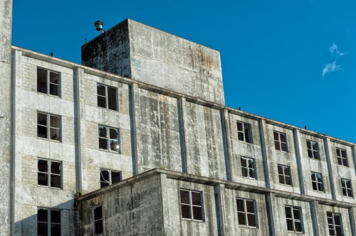 Abandoned building with weathered concrete walls and multiple empty windows against a clear blue sky.