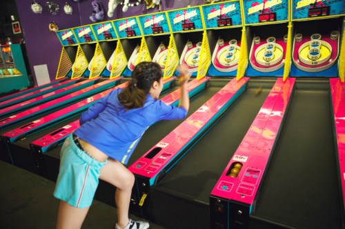 A child plays a skee-ball game in an arcade, aiming for the targets with enthusiasm.