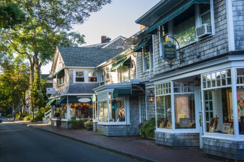 Charming street lined with quaint shops featuring shingled facades and colorful window displays under a clear blue sky.