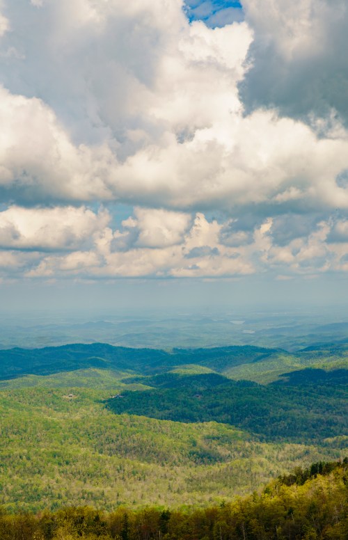 A panoramic view of lush green mountains under a cloudy sky, showcasing rolling hills and distant valleys.