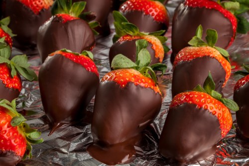 A close-up of fresh strawberries dipped in rich chocolate, arranged on a shiny surface.