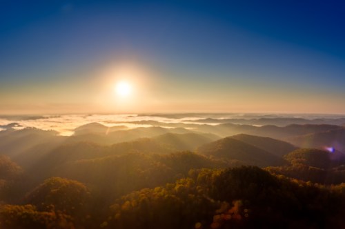 A breathtaking sunrise over misty mountains, with soft light illuminating the landscape and a clear blue sky above.