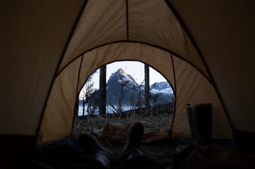 View from inside a tent, showcasing a mountain landscape at dawn with snow-capped peaks and a serene atmosphere.
