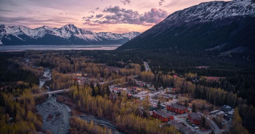 Sunset over the town of Girdwood, showing buildings nestled in a valley beside a winding river.