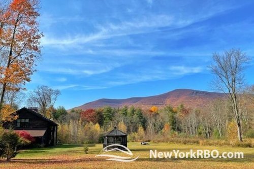 A scenic view of a house and gazebo surrounded by autumn foliage and mountains under a clear blue sky.