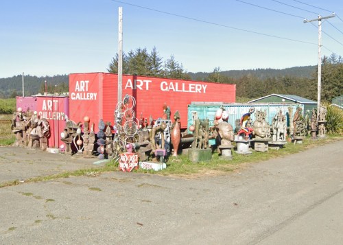Colorful outdoor art gallery featuring various sculptures displayed around shipping containers in a rural setting.