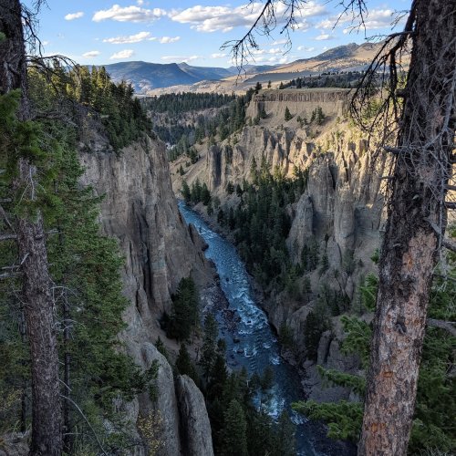 A scenic view of a river winding through rocky cliffs, surrounded by trees and mountains under a blue sky.