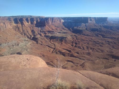 A vast desert landscape with red rock formations and canyons under a clear blue sky.