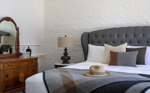 Cozy bedroom featuring a tufted bed, decorative pillows, a vintage dresser, and a straw hat on a blanket.