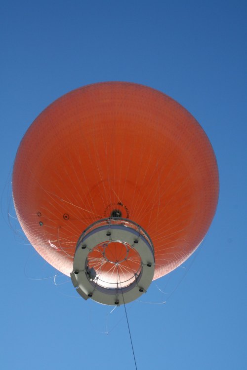 A large orange hot air balloon against a clear blue sky, viewed from below.