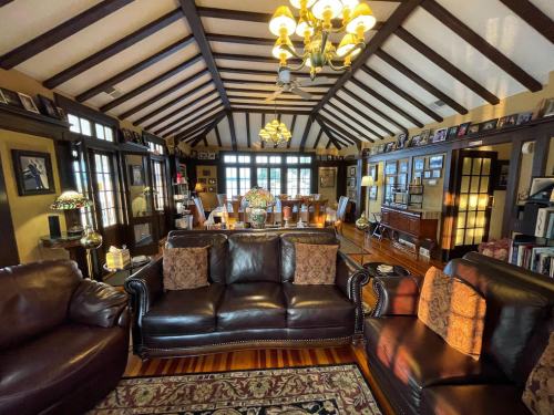Cozy living room with wooden beams, leather sofas, and a dining area, adorned with photos and warm lighting.