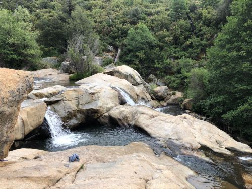 A serene rocky landscape with a flowing stream and lush greenery surrounding the water.