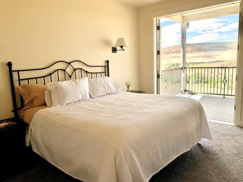 Bright bedroom with a white bedspread, nightstand, and a balcony door opening to a scenic view.