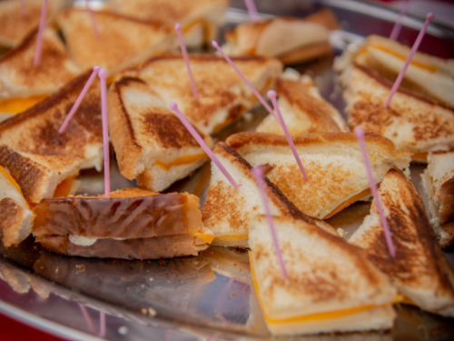 A platter of toasted sandwiches with cheese, some cut into triangles and held together with pink toothpicks.