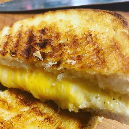 Close-up of a golden-brown grilled cheese sandwich, with melted cheese oozing between crispy toasted bread.