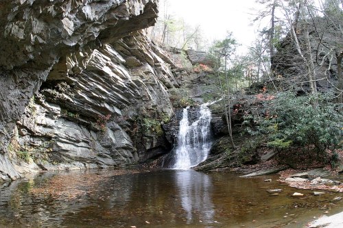 A serene waterfall cascades into a calm pool, surrounded by rocky cliffs and lush greenery.