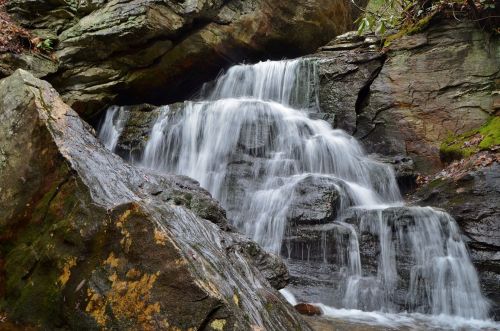 A serene waterfall cascading over rocky ledges, surrounded by lush greenery and moss.
