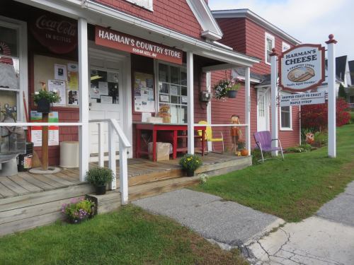 A quaint country store with a red exterior, porch seating, and a sign for Harman's Cheese in a rural setting.