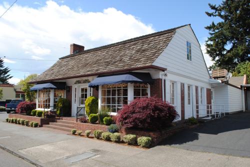 A charming white house with a sloped roof, large windows, and colorful landscaping on a sunny day.