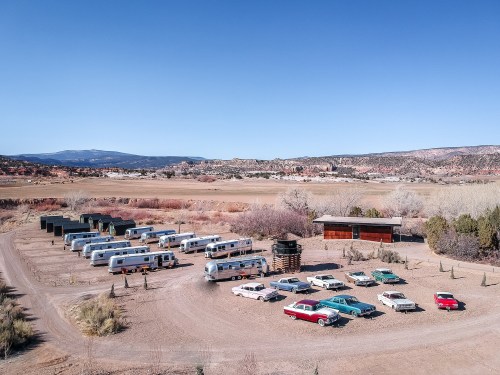 Aerial view of a vintage trailer park with classic cars, surrounded by desert landscape and mountains in the background.