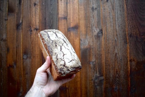 A hand holding a rustic loaf of bread against a wooden background.