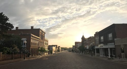 A quiet street at sunset, lined with historic buildings and a colorful sky, creating a serene atmosphere.