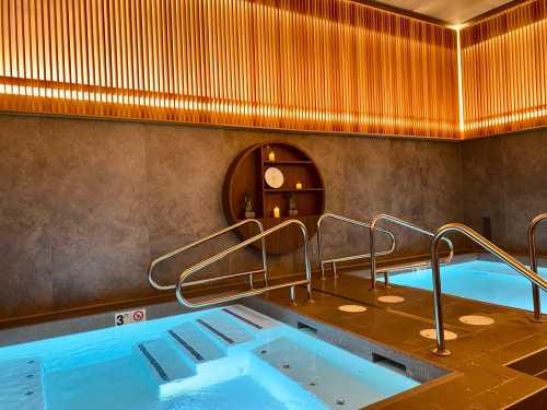 A serene spa area featuring two hot tubs with blue water, wooden accents, and soft lighting.