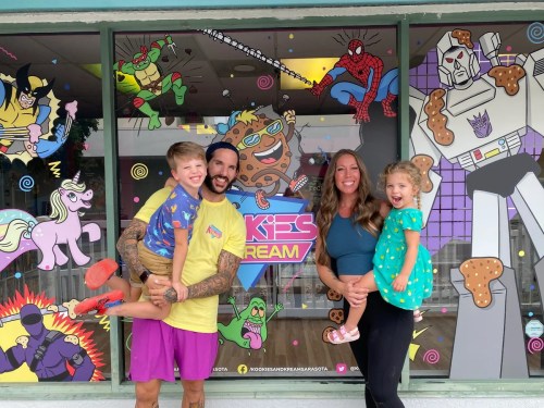A family of four poses outside a colorful shop with cartoon characters on the window, smiling and enjoying their time together.