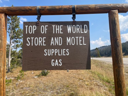 Sign for "Top of the World Store and Motel" indicating supplies and gas available, set against a rural landscape.