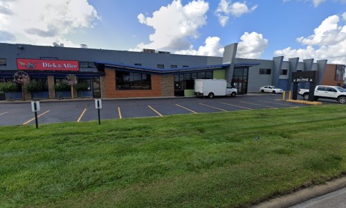 A storefront with "Dick & Alice" sign, surrounded by green grass and a clear blue sky with clouds.