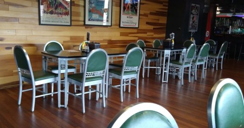 A spacious restaurant interior with green chairs and wooden walls, featuring empty tables and vintage movie posters.