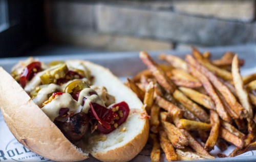 A hot dog topped with jalapeños and mustard, served with a side of crispy French fries.