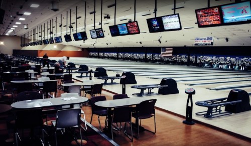 A spacious bowling alley with empty lanes, tables, and screens displaying scores.