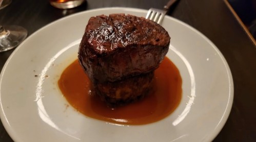 A perfectly cooked piece of beef steak on a white plate, drizzled with rich brown sauce.