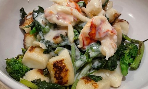 A bowl of gnocchi topped with lobster, sautéed greens, and a creamy sauce.