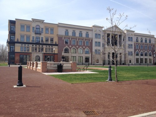 Modern multi-story building with a mix of brick and stucco, surrounded by green grass and pathways.