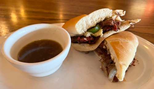 A plate with a sandwich filled with shredded meat and peppers, alongside a small bowl of dipping sauce.