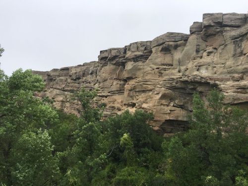 Rocky cliffs rise above lush green trees under a cloudy sky.