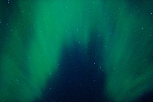 A vibrant green aurora borealis lights up the night sky, filled with stars against a dark backdrop.