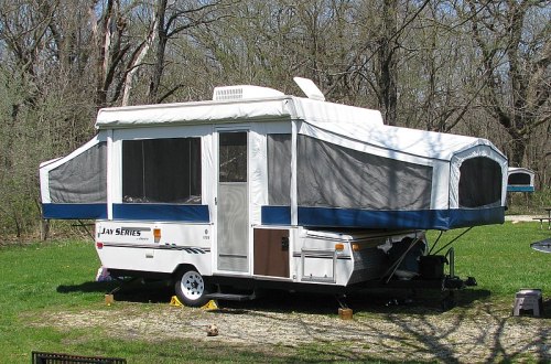 A pop-up camper parked on a grassy area, surrounded by trees, with a blue and white exterior.