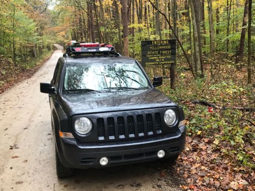 A black SUV parked on a dirt road near a sign for Yellowwood State Forest, surrounded by autumn foliage.