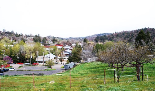 A scenic view of a small town surrounded by hills, with green fields and trees in the foreground.