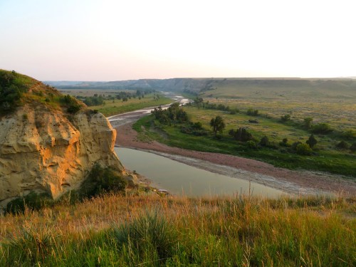 A scenic view of a winding river surrounded by green hills and rocky cliffs at sunset.